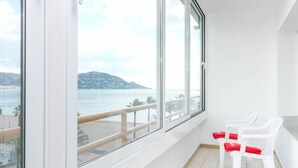 En balkon med store vinduer med udsigt over kysten, hvide stole og flisegulv.