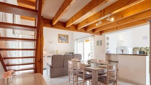 Un coin repas avec une table et des chaises en bois, un canapé et, au fond, une cuisine.
