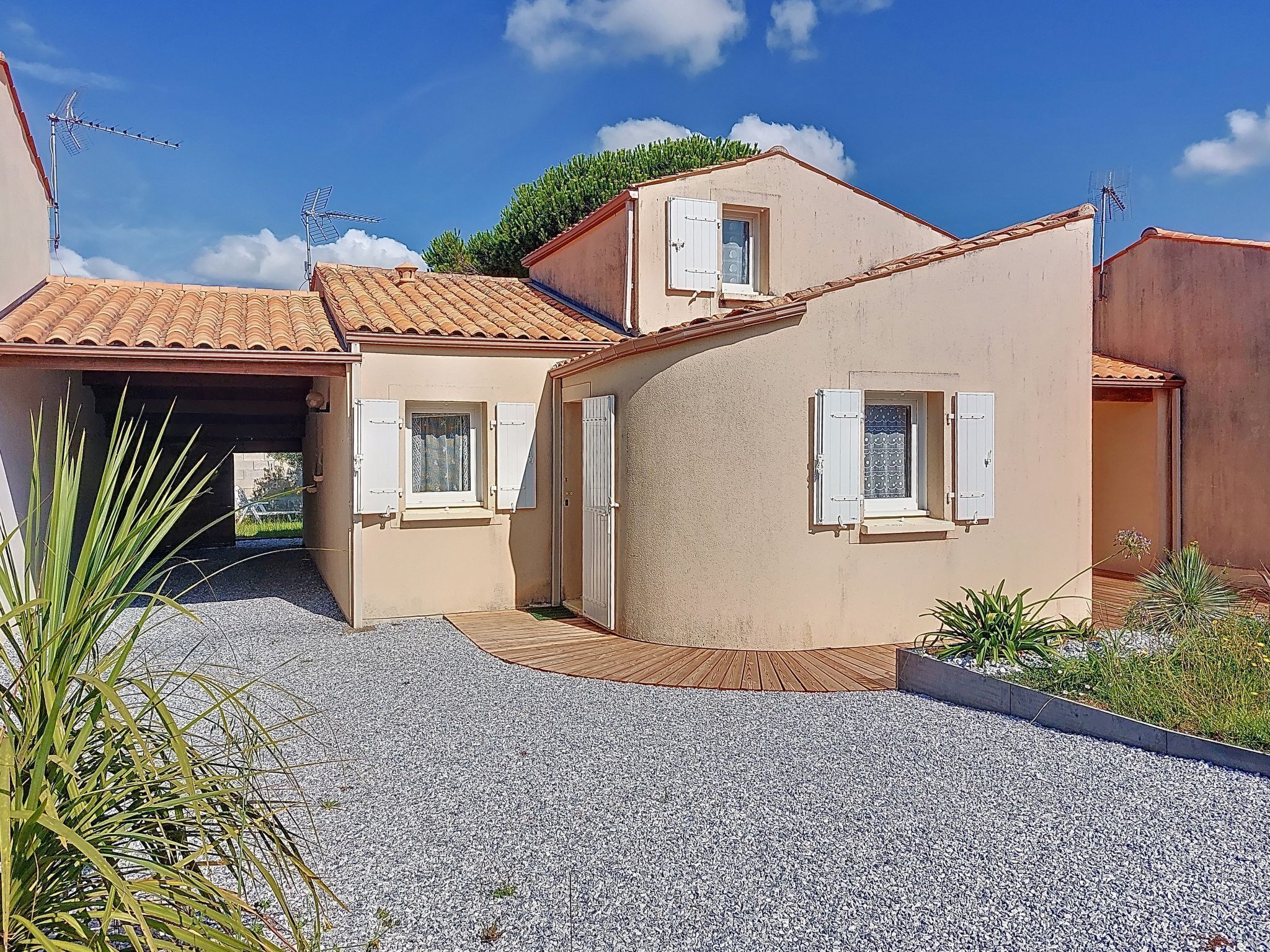A two-story building with a tiled roof, a gravel driveway, and a small garden area.
