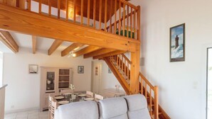 Un vaste espace de vie agrémenté d’un grand escalier en bois, d’une table à manger avec des chaises, et d’un coin salon confortable avec des canapés.