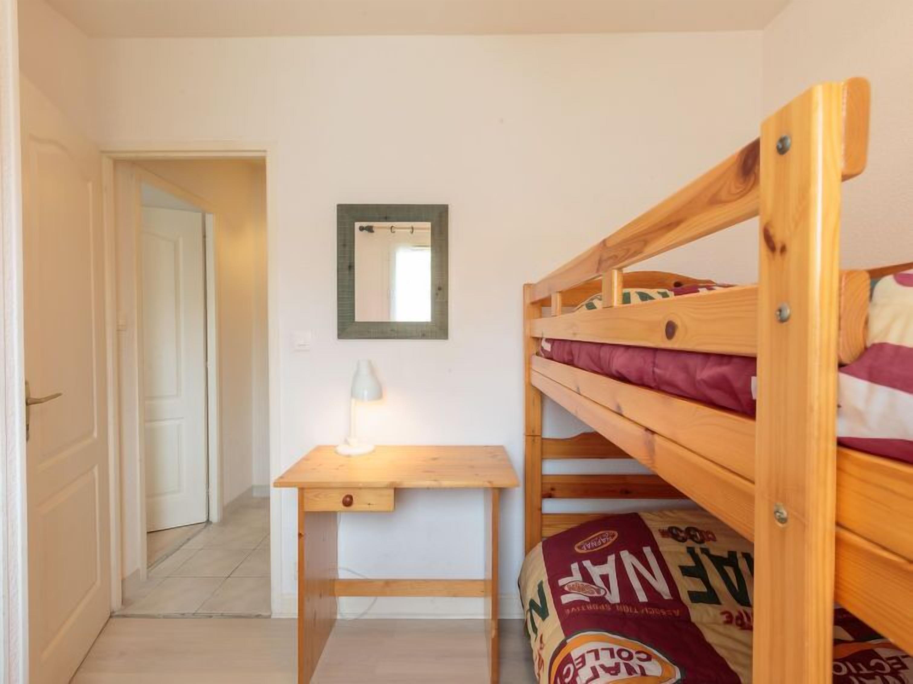 A small room with a bunk bed, a desk with a lamp, and a mirror on the wall.