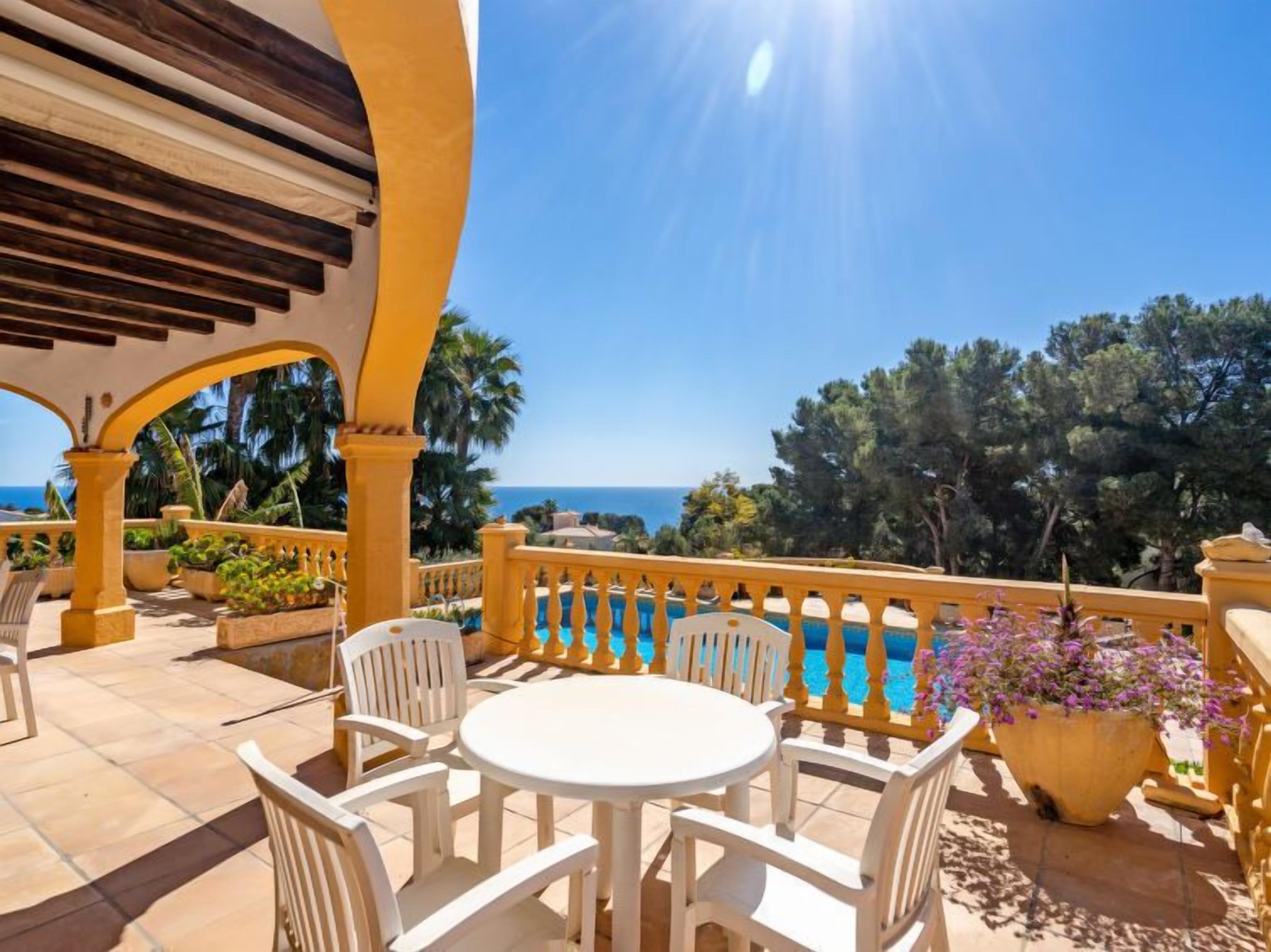 Une terrasse avec une table ronde et des chaises, donnant sur une piscine et la mer.