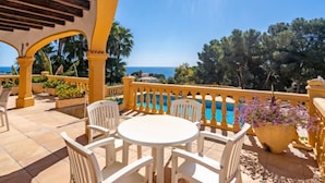 Eine Terrasse mit rundem Tisch und Stühlen, mit Blick auf einen Pool und das Meer.