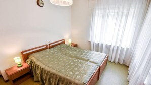 A bedroom with a bed, two bedside tables with lamps, a clock on the wall, and a window with white curtains. - La Busa by Interhome (Alleghe)