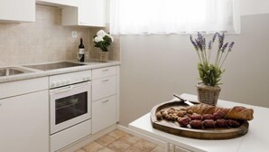 A kitchen with white cabinets, a sink, a stove, and a window with sheer curtains. - Double Room by Interhome (Ascona)
