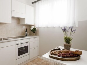 A kitchen with white cabinets, a sink, a stove, and a window with sheer curtains.