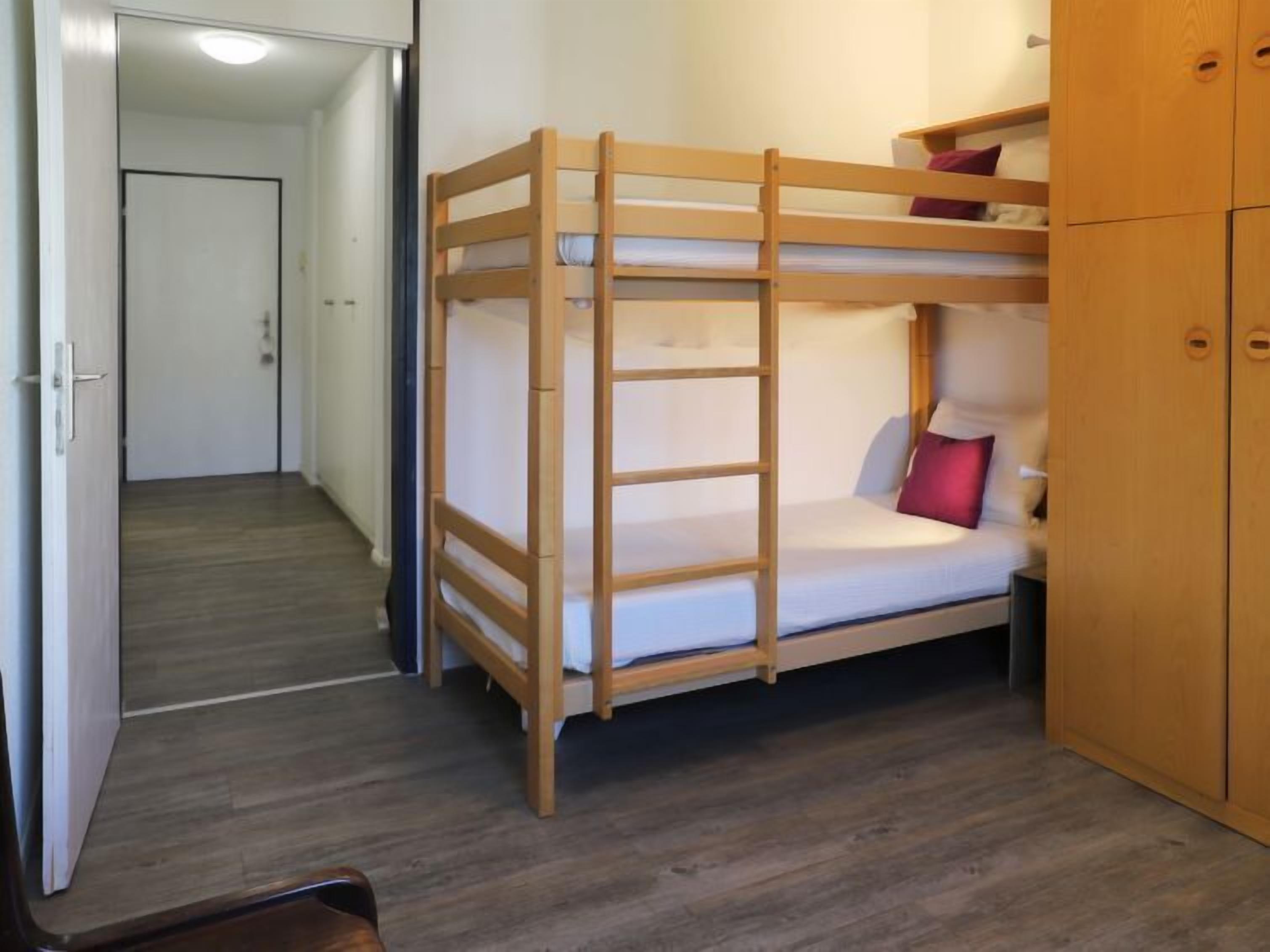 A bunk bed room with a wooden ladder, a wardrobe, and a door leading to another room.