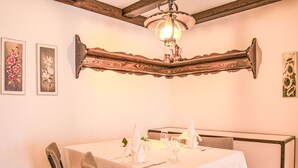 A dining area with a table set for two, wooden chairs, a chandelier, and floral wall art. - Residenz Surlej 6 by Interhome (St. Moritz)