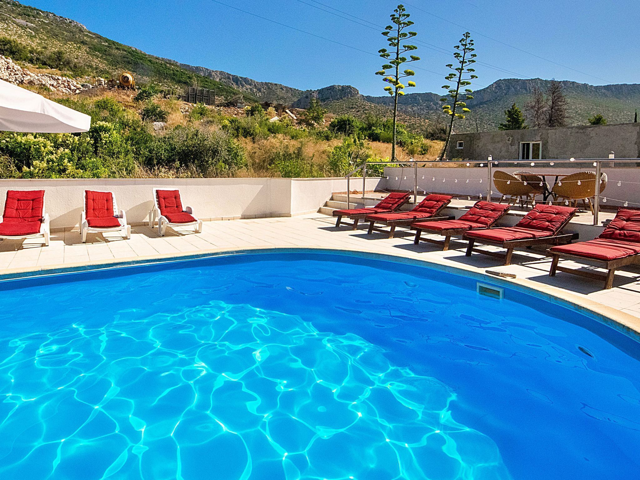 A swimming pool with clear blue water, surrounded by red lounge chairs and a small building in the background.