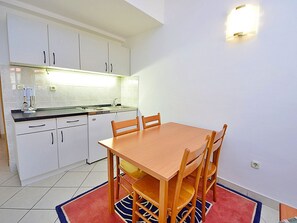Une cuisine de taille modeste, avec des meubles blancs, une table à manger en bois et un tapis rouge.