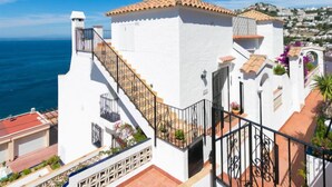 Un bâtiment blanc avec un toit recouvert de tuiles, un escalier menant à un balcon et une vue sur la mer.