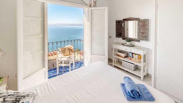 Une chambre avec un lit, une petite coiffeuse avec un miroir et une vue sur la mer.