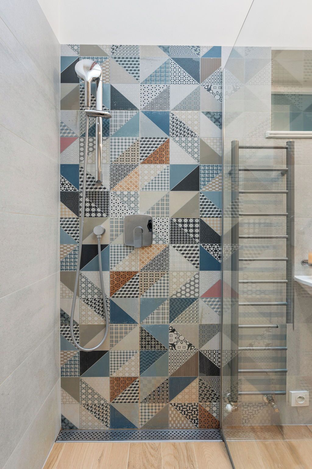 Une douche avec un carrelage aux motifs géométriques, une porte en verre et un porte-serviettes en métal.