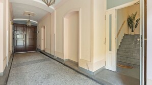 A hallway with a stone floor, a staircase with a potted plant, and a door at the end. - Apartment O21 by Interhome (Prague centre)