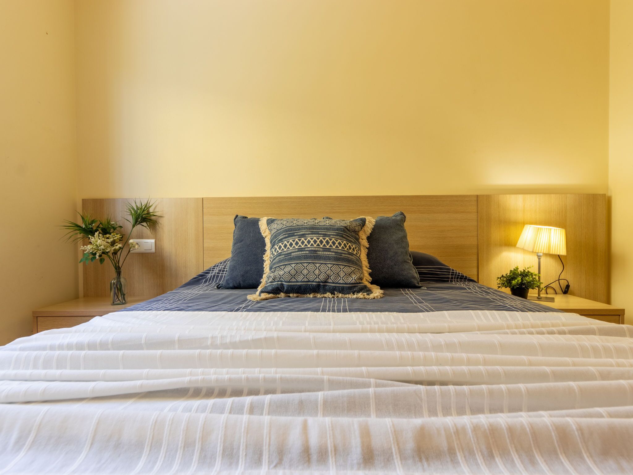 Una cama bien hecha con una colcha estampada, un cabecero de madera y una lámpara de noche.