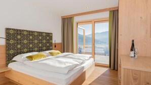 Habitación de hotel moderna con una cama grande, cabecera de madera y vistas a las montañas a través de una puerta corrediza de vidrio.