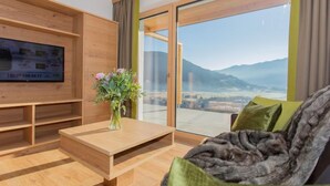Un salón moderno con un mueble de televisión de madera, una mesa de centro y un sofá con cojines verdes. Un jarrón con flores está sobre la mesa de centro.