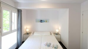 Una camera d'albergo con un letto grande, due comodini, una lampada a soffitto, una finestra con tende e un quadro appeso al muro.