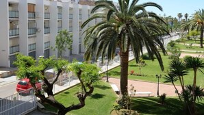 Un edificio moderno con balconi e un giardino curato con palme e arbusti.