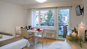 Ein modernes Hotelzimmer mit Essbereich, einem Balkon mit Blick auf Gebäude und Bäume sowie einem an der Wand befestigten Fernseher.