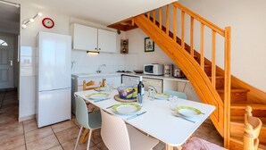 Een compacte keuken met witte kastjes, een houten trap en een eethoek met een tafel voor twee personen.