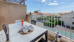 Een balkon met een tafel gedekt voor vier personen, stoelen en uitzicht op zee en gebouwen.