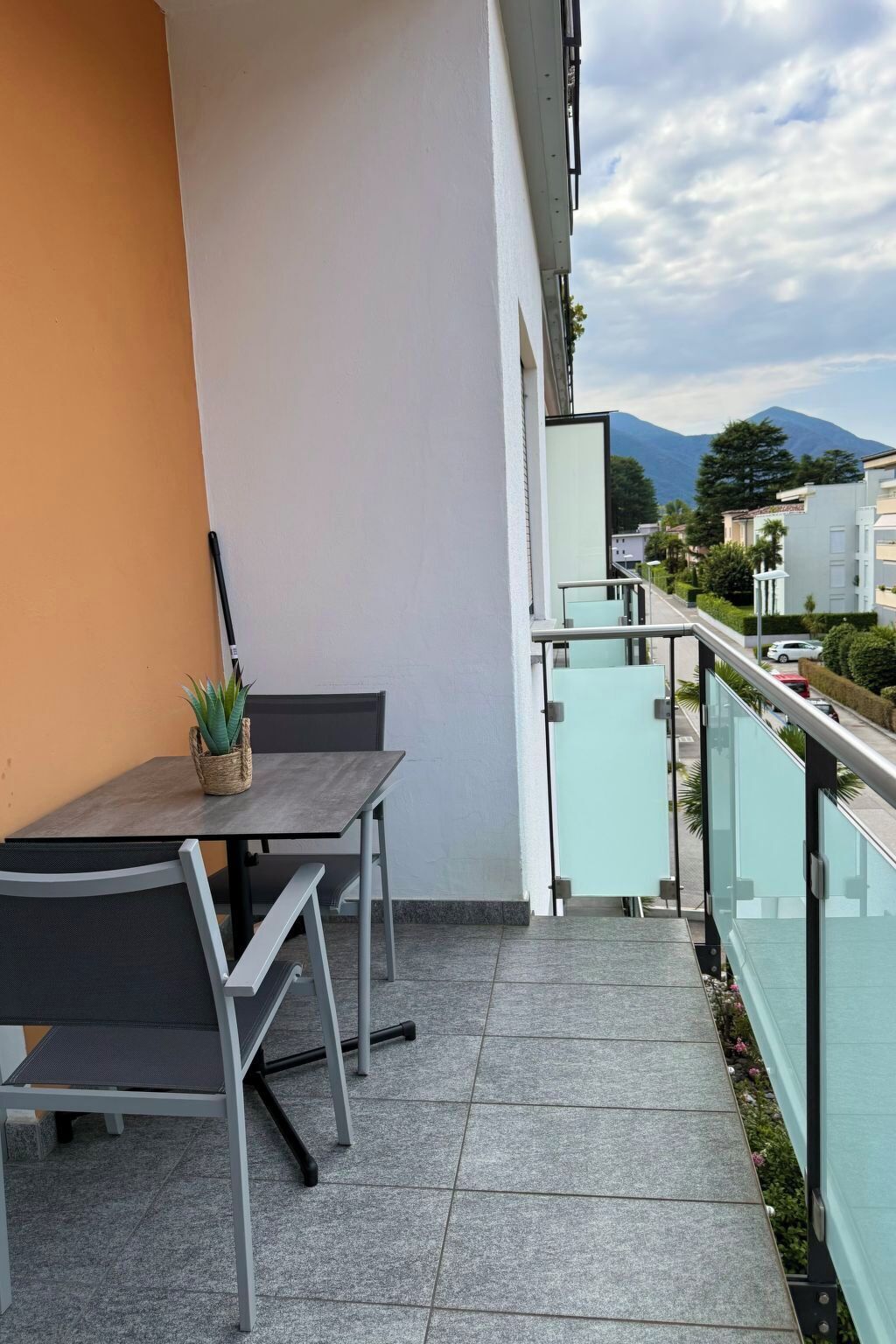 Ein Balkon mit Tisch und Stühlen, einem Blumentopf und Blick auf einen Berg und Gebäude.