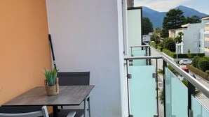 Un balcone con tavolo e sedie, una pianta in vaso e vista su una montagna e degli edifici.
