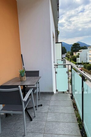 A balcony with a table and chairs, a potted plant, and a view of a mountain and buildings.