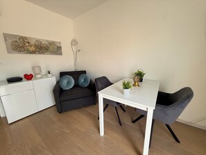 A modern living space with a white dining table, a black sofa with blue cushions, a white cabinet, and a decorative wall piece.