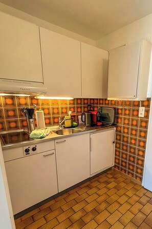 A compact kitchen with white cabinets, a stainless steel sink, and a patterned backsplash.