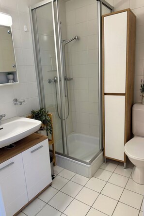 A bathroom with a shower enclosure, a sink, a toilet, and a cabinet.