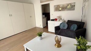 Un soggiorno moderno con un tavolo bianco, un divano nero con cuscini blu e una cucina sullo sfondo.
