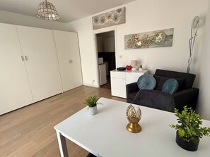 A modern living room with a white table, a black sofa with blue cushions, and a kitchen in the background.