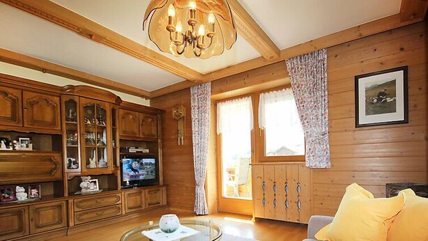 A cozy living room with wooden paneling, a glass coffee table, a sofa with yellow cushions, and a television on a wooden cabinet.