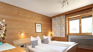 A wooden-paneled bedroom with a bed, bedside tables, a framed picture, and a window with curtains.