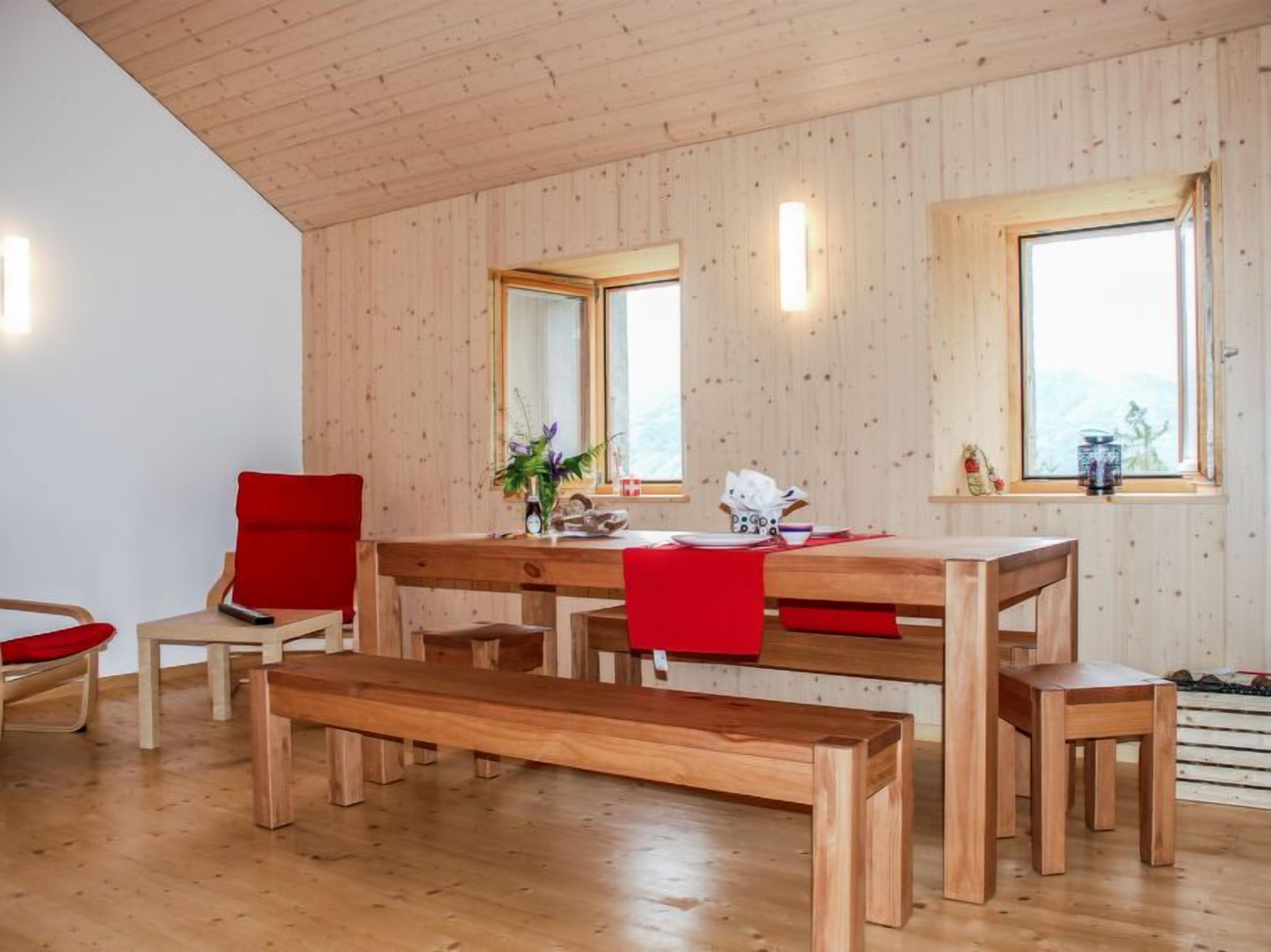 Un intérieur en bois avec une table à manger, des bancs et des chaises rouges.