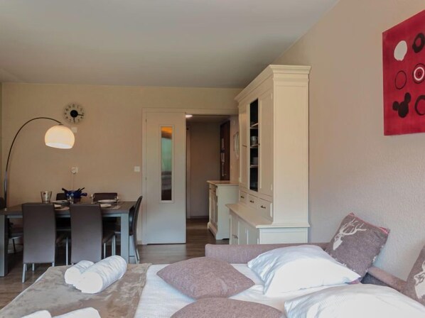 A bedroom with a bed, a desk, and a chair. There is a wardrobe and a door leading to another room.
