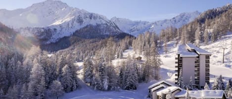 A snow-covered mountain landscape with a lodge featuring a ski lift and a clear view of the surrounding peaks.