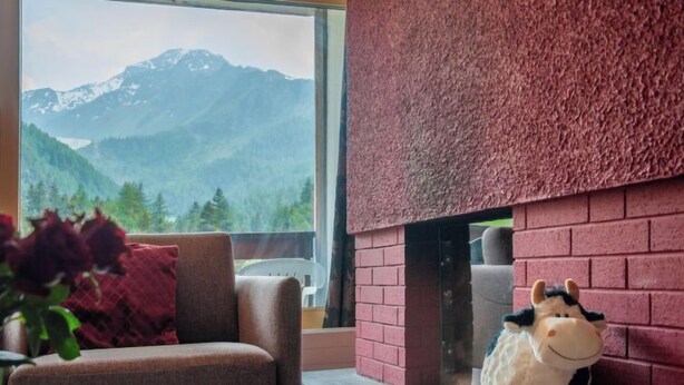 A cozy room with a view of mountains, a brick fireplace, a plush toy, and a red cushion on a chair. - Rosablanche C51 by Interhome (Siviez-Nendaz)