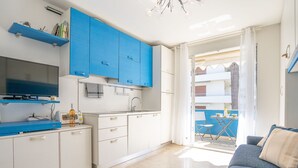 Una cocina compacta con armarios azules, un comedor con mesa y sillas, y vistas al balcón exterior.