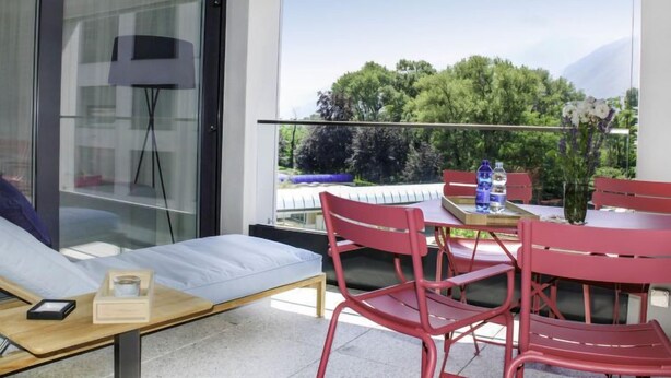 Un balcon moderne avec un canapé, des chaises rouges et une table agrémentée d’un vase de fleurs.
