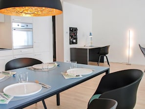 A modern kitchen with white cabinets, a built-in oven, and a dining area with a long table set for four.
