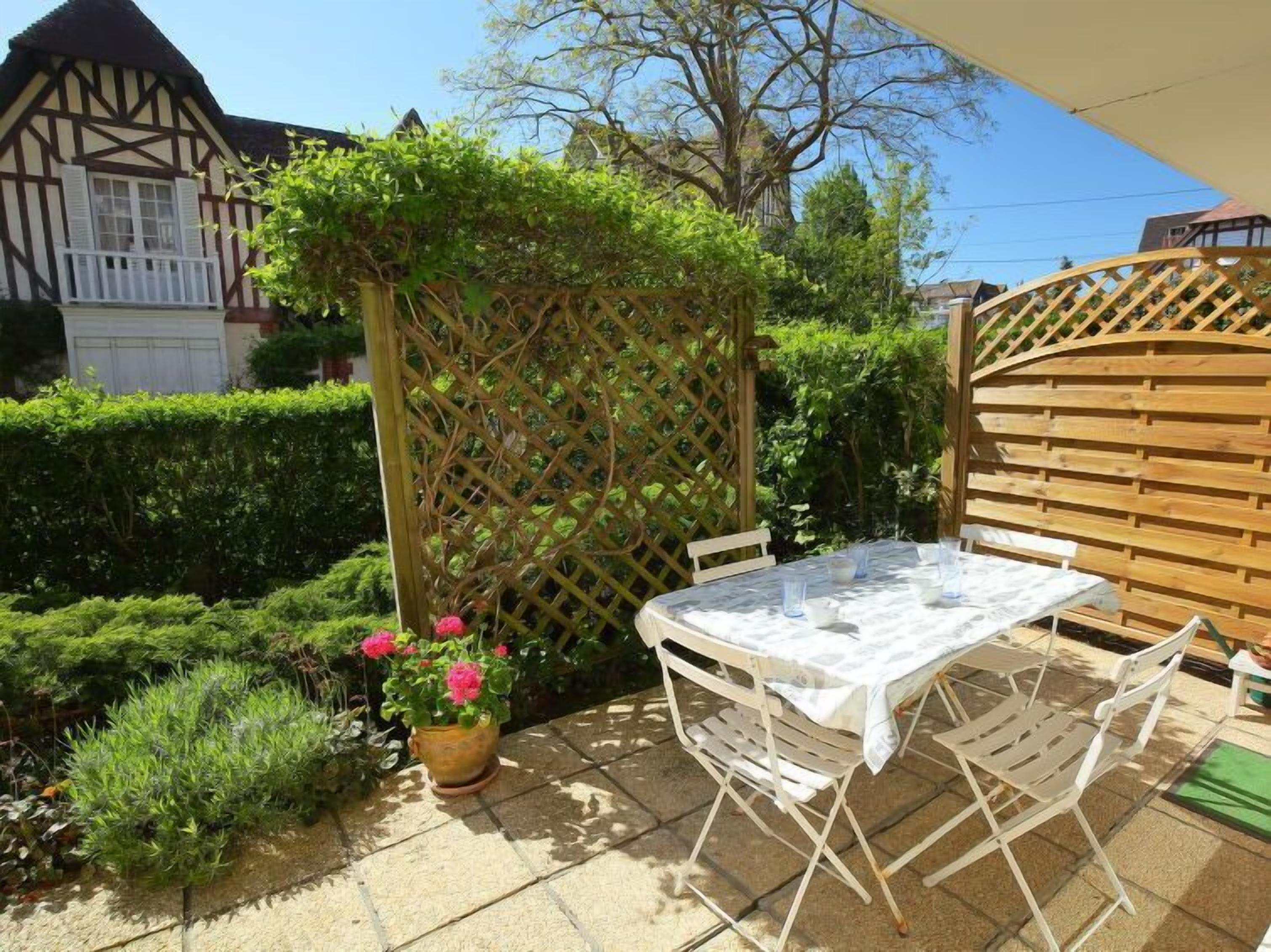 Eine Terrasse mit Tisch und Stühlen, umgeben von einem Holenzaun und Pflanzen.
