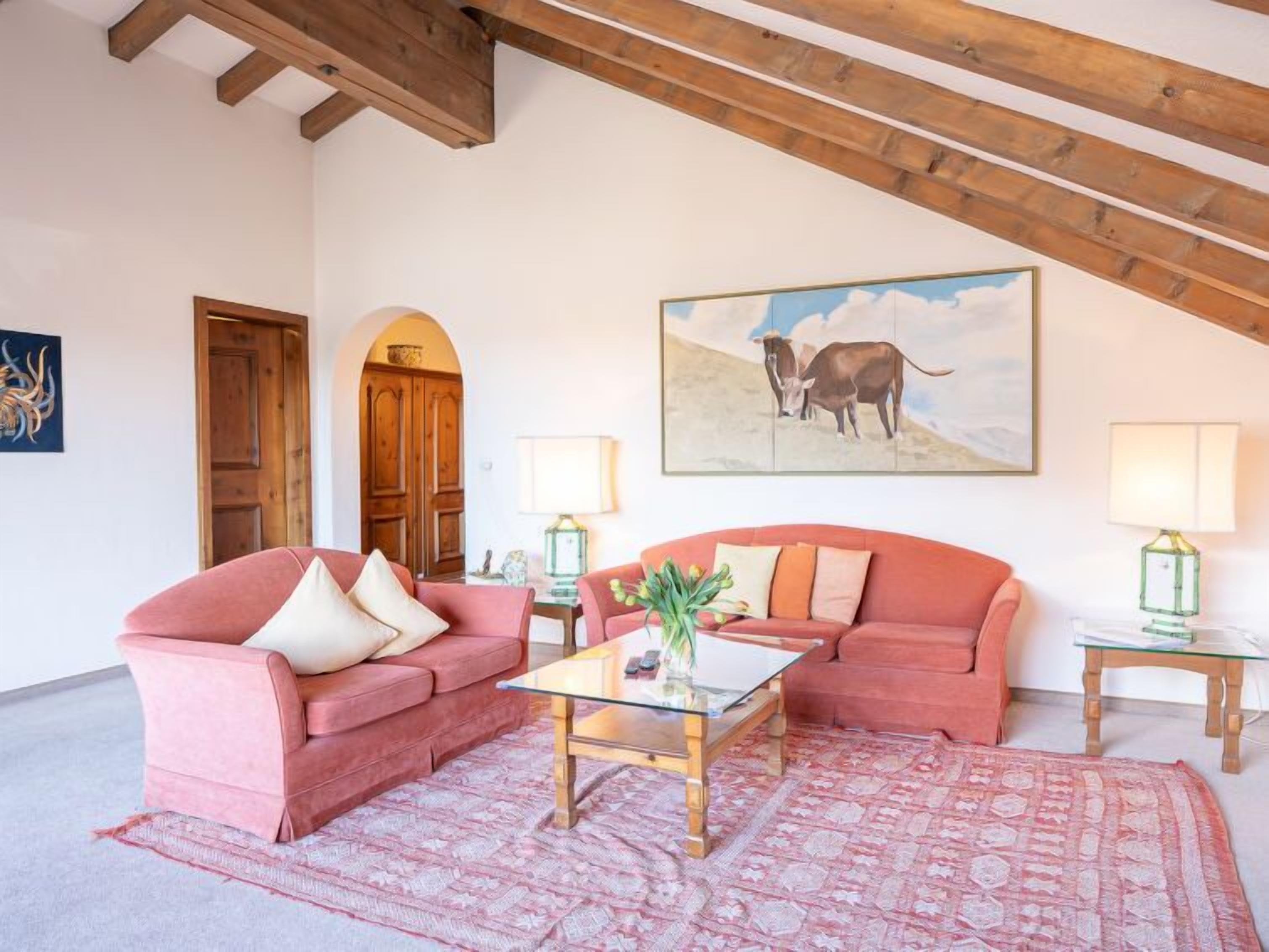 Ein gemütliches Wohnzimmer mit zwei roten Sofas, einem Glastisch und einem Bild von Kühen an der Wand.