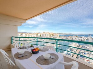 Ein Balkon mit Tisch für zwei Personen mit Blick auf eine Marina, in der Boote und Gebäude zu sehen sind.