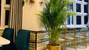 A modern interior with teal chairs, a large potted plant, and a wall with leaf and insect art. - KGI Mountainside Hotel (Lagawe)