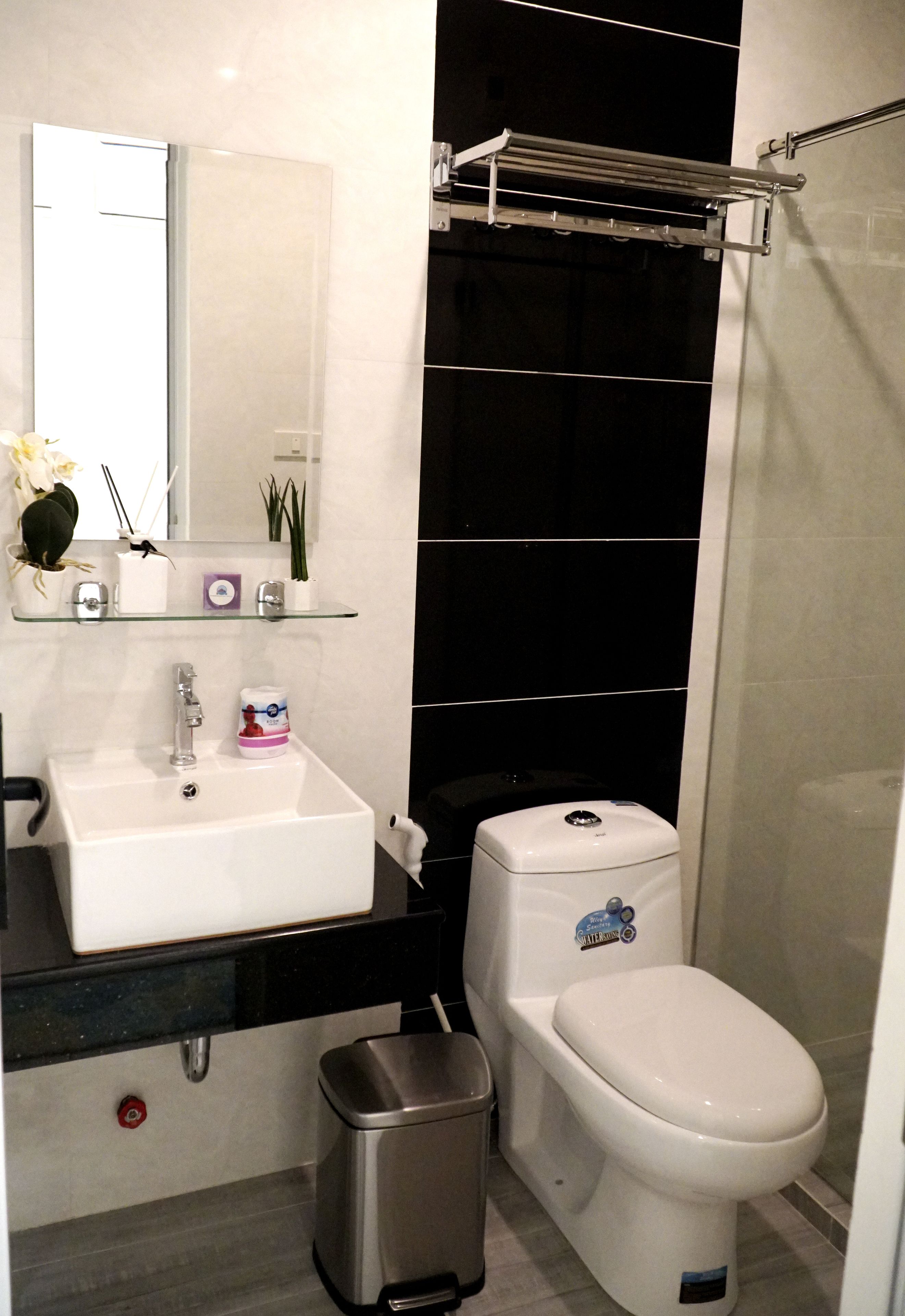 A modern bathroom with a white sink, mirror, and toilet. There is a trash bin and a towel rack.
