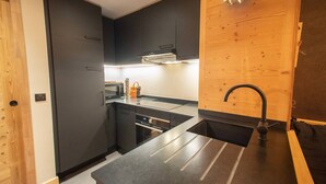A modern kitchen with dark cabinetry, a stainless steel countertop, and a wooden accent wall. - 5-room duplex for 10 guests with balcony, Hameau de la Forêt (Valmorel)