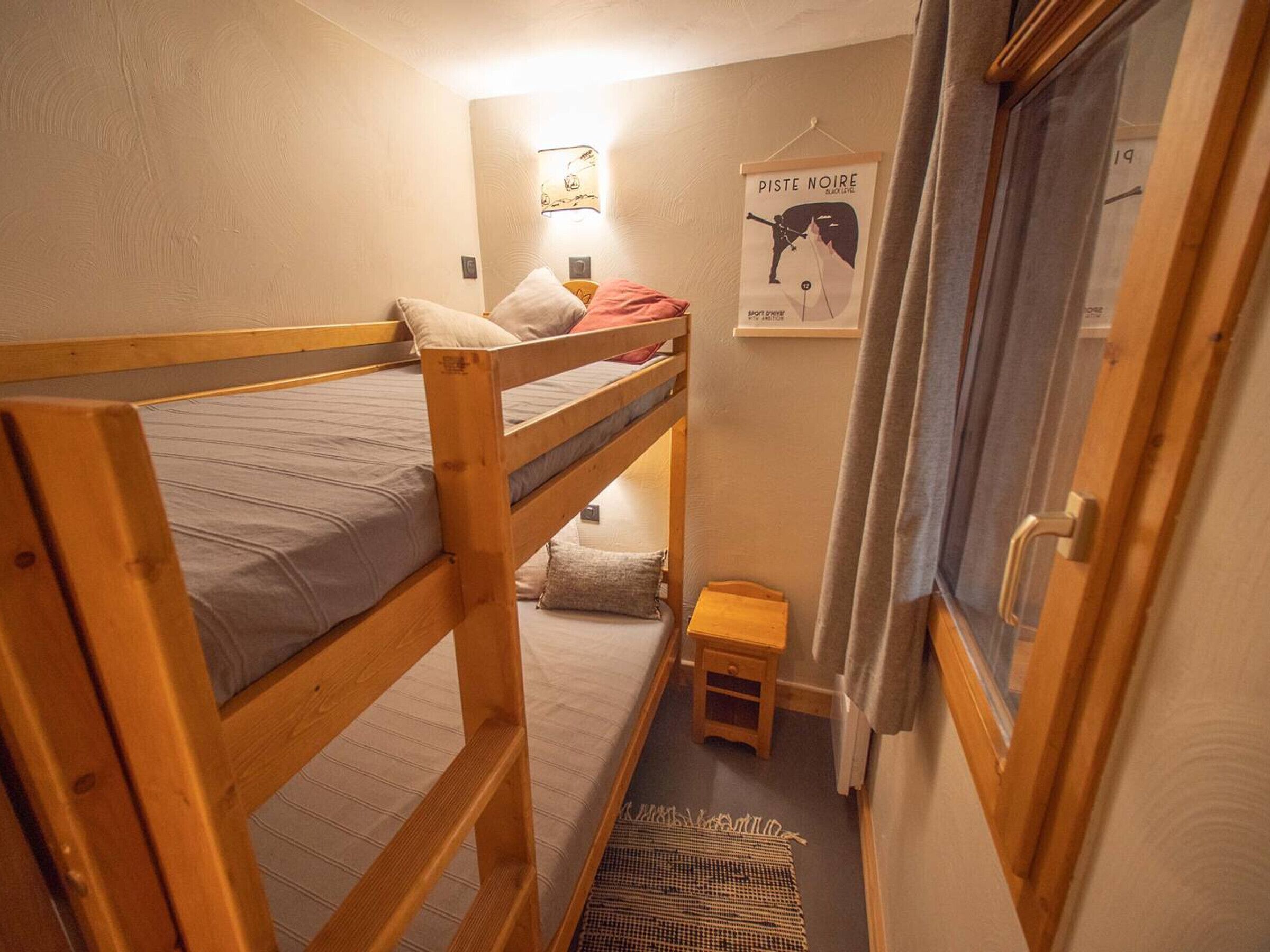 Une chambre avec un lit superposé, un petit tabouret en bois et une affiche accrochée au mur.